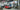A vintage red car undergoing restoration in a well-equipped workshop with various tools and auto parts.