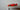 Side view of a red toy race car displayed on a wooden shelf indoors.